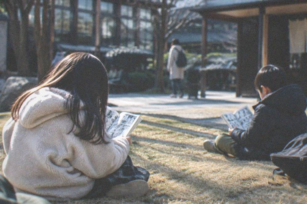 Children sitting on a courtyard lawn reading manga books