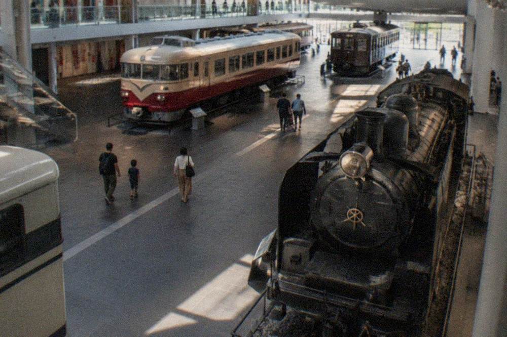 A modern museum entrance hall with a large suspended railway sign and visitors at ticket gates