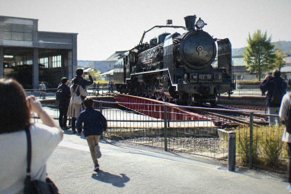 A polished black steam locomotive on a turntable surrounded by museum visitors taking photographs