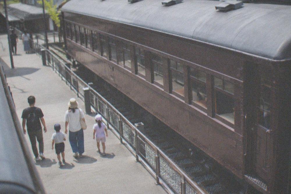 A family walking along a museum platform beside a vintage passenger carriage on a sunny morning
