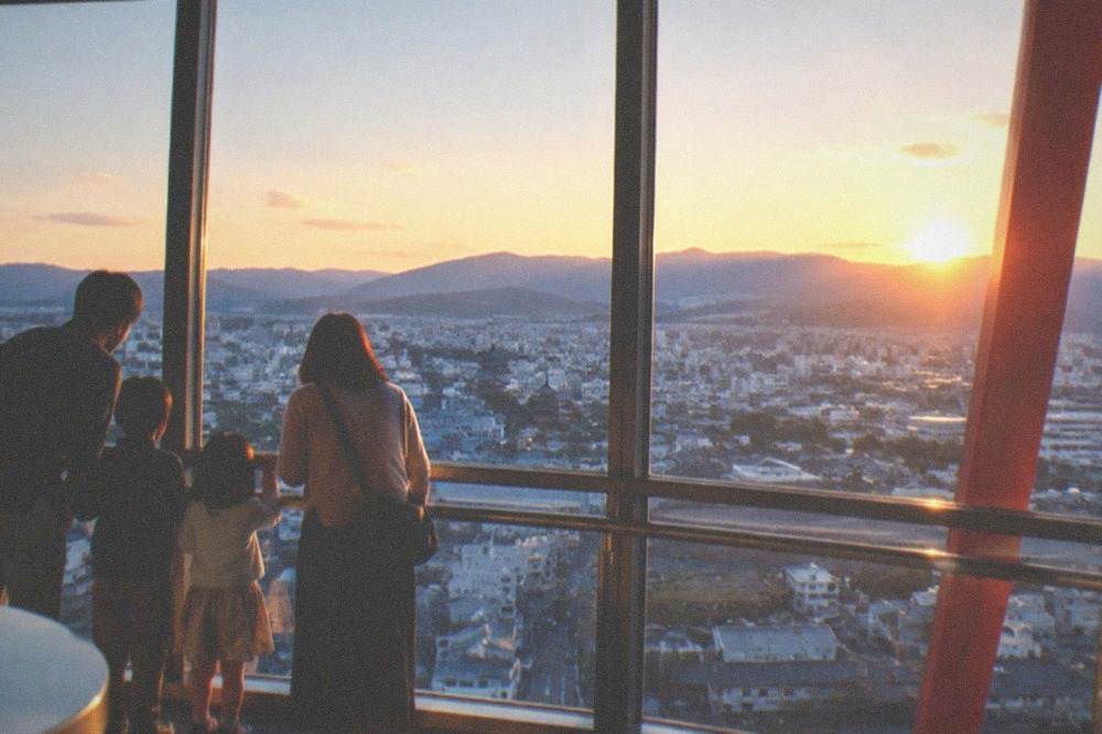 Families with children looking out through the observation deck's windows toward the city
