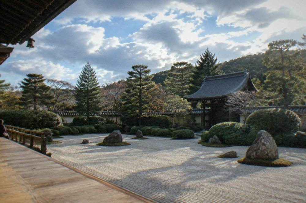 A raked gravel Zen garden with clipped shrubs and a wooden temple veranda in soft morning light