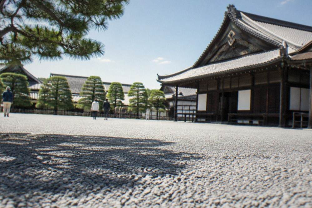 A wide gravel courtyard inside Nijo Castle with palace buildings and pine trees