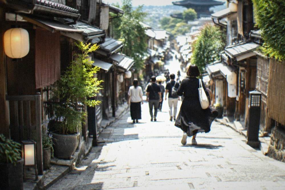 Visitors walking down the stone-paved Ninenzaka lane past lantern-lit wooden shopfronts