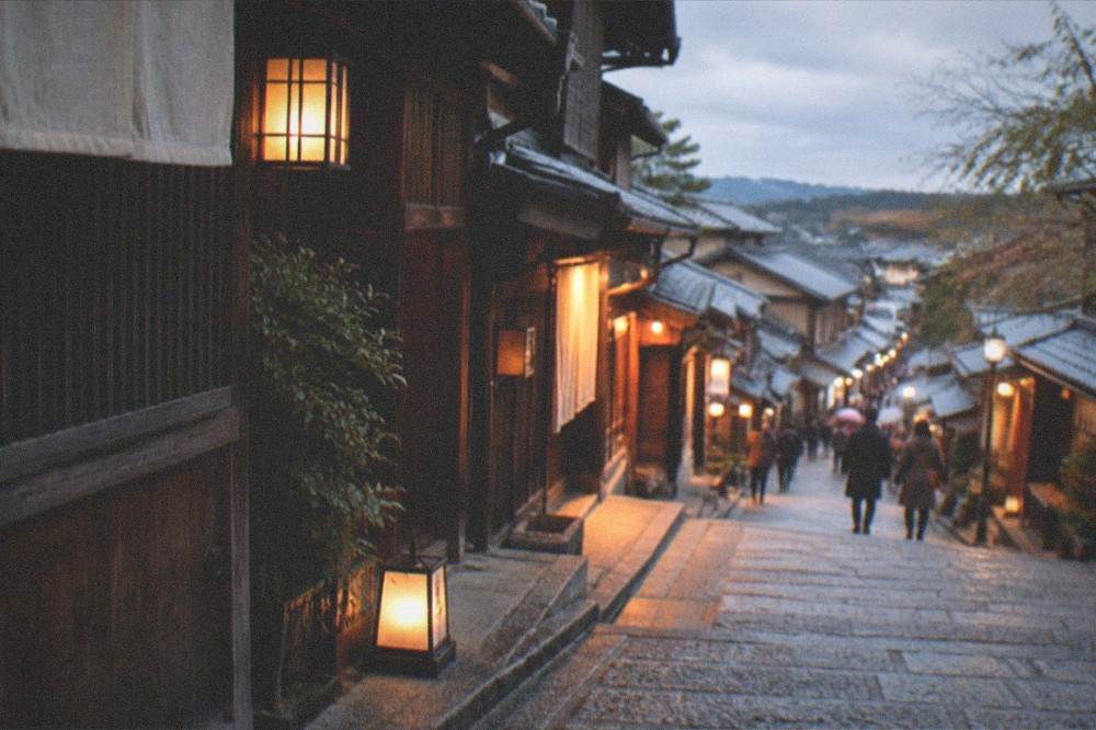 Evening light on the stone slope with lanterns glowing outside closed wooden shopfronts