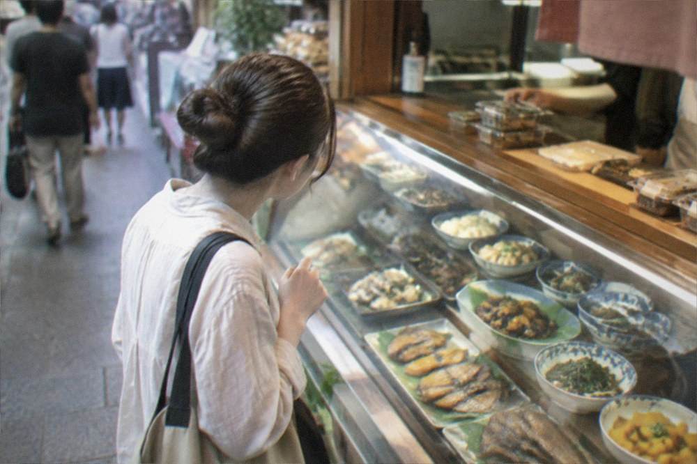 A shopper buying food at a market counter with displayed dishes behind glass