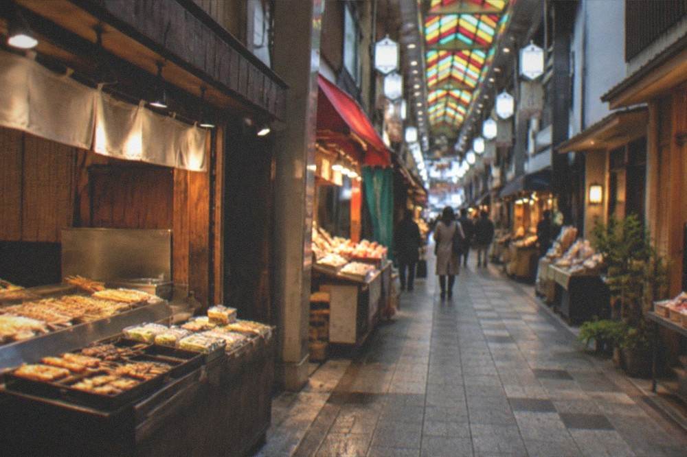 The covered market arcade at dusk with stall lights on and few shoppers remaining