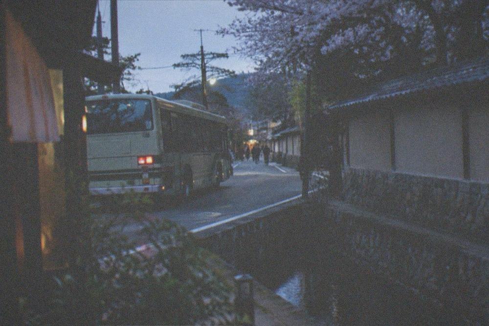 A city bus passing a narrow street with a temple wall in Kyoto