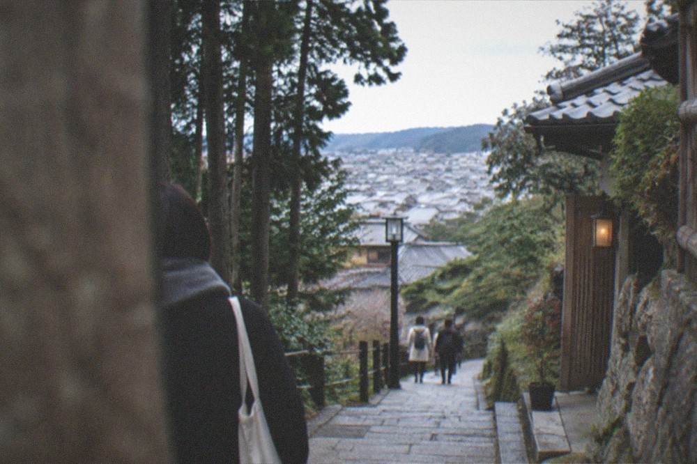 A hillside trail through cedar forest above a village of traditional houses