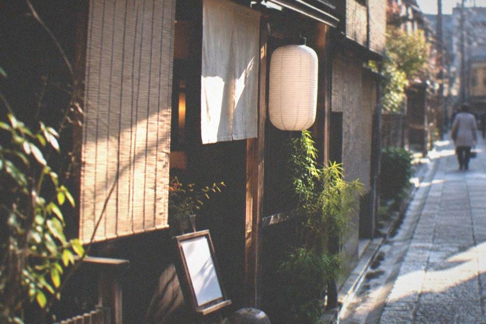 A small restaurant entrance with a paper lantern, bamboo blinds and a handwritten menu on display