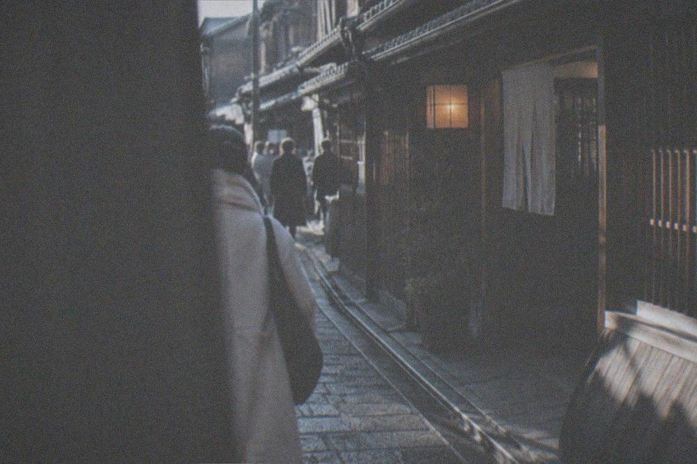 A traditional wooden machiya facade with lattice windows and a stone path leading to a lit entrance