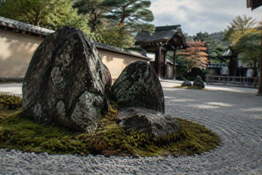 Close view of a cluster of dark weathered stones surrounded by moss on raked white gravel in a Zen garden
