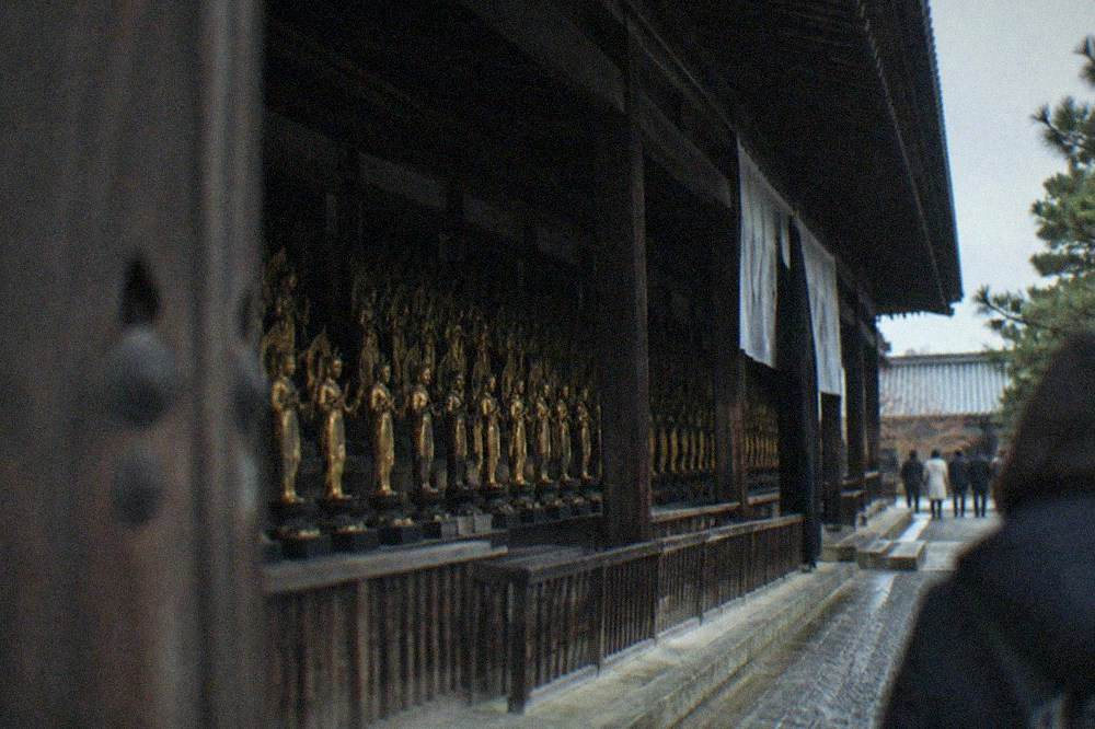 Rows of small gilded statues on stepped platforms receding into a dark temple interior