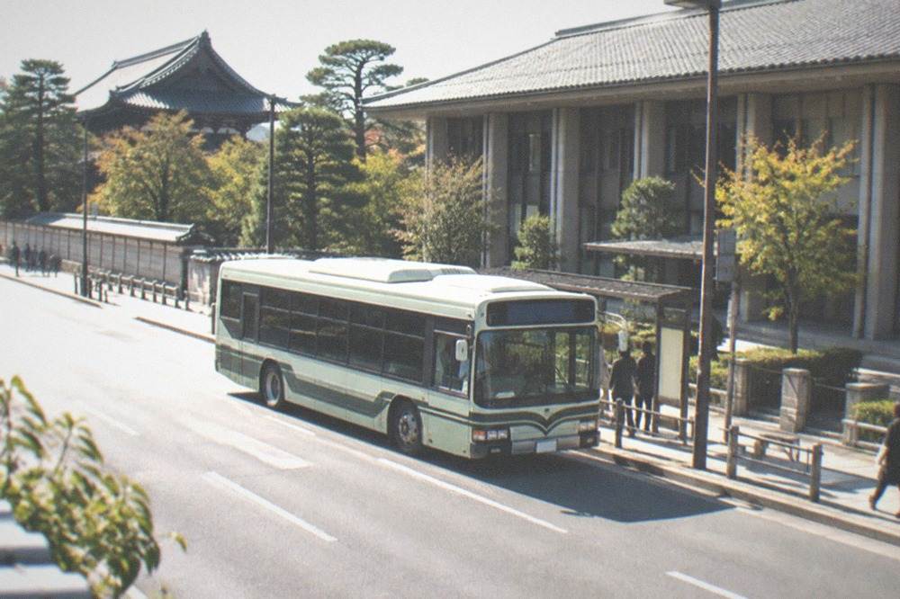 A city bus stopped at a kerb on a wide street with a museum building behind it