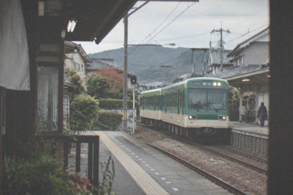 A two-car Eizan Railway local train at a small station in residential Kyoto