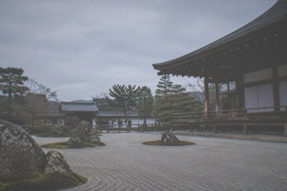 A stone rock garden with raked gravel and a wooden temple veranda in the background