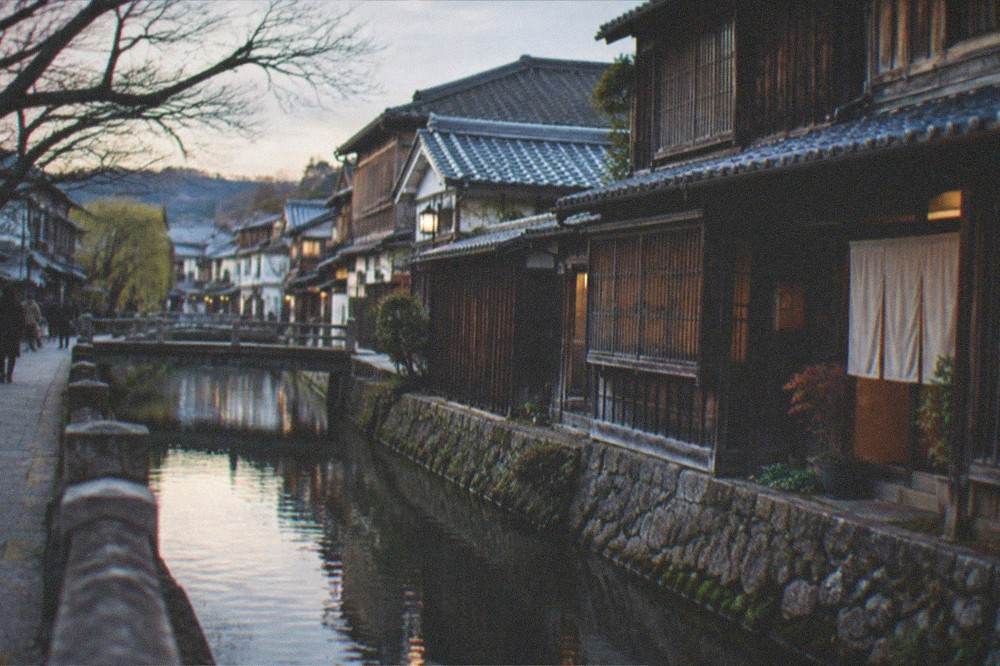 Wooden brewery buildings along a quiet canal street in a Kyoto sake district at dusk