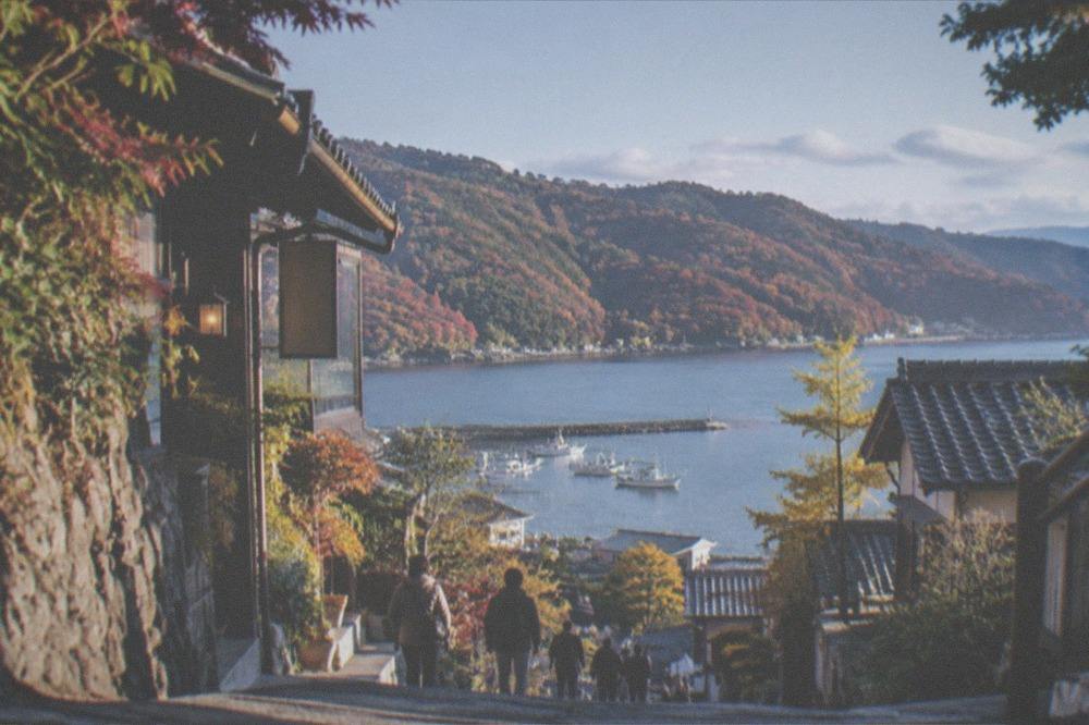 Autumn colours on hillsides above a calm coastal bay with fishing boats