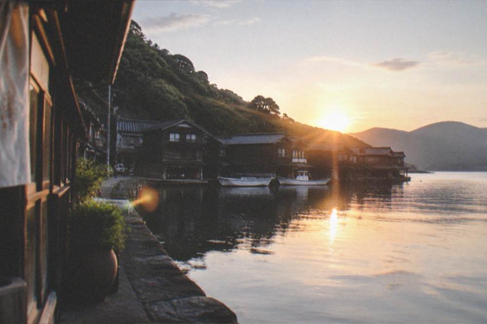 A calm bay at dusk with dark wooden boathouses reflected in still water