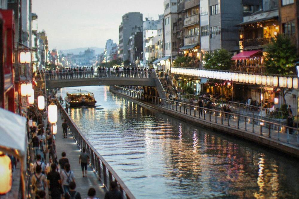The illuminated Dotonbori canal in Osaka at night, with crowds on the bridges and neon signs above the water