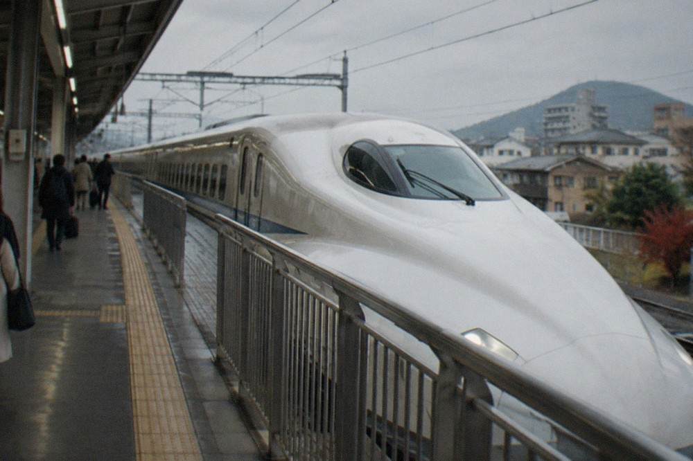 A white Shinkansen bullet train waiting at a station platform beside a signboard