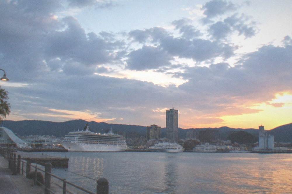 A harbor skyline with cruise ships and city buildings seen across water at dusk