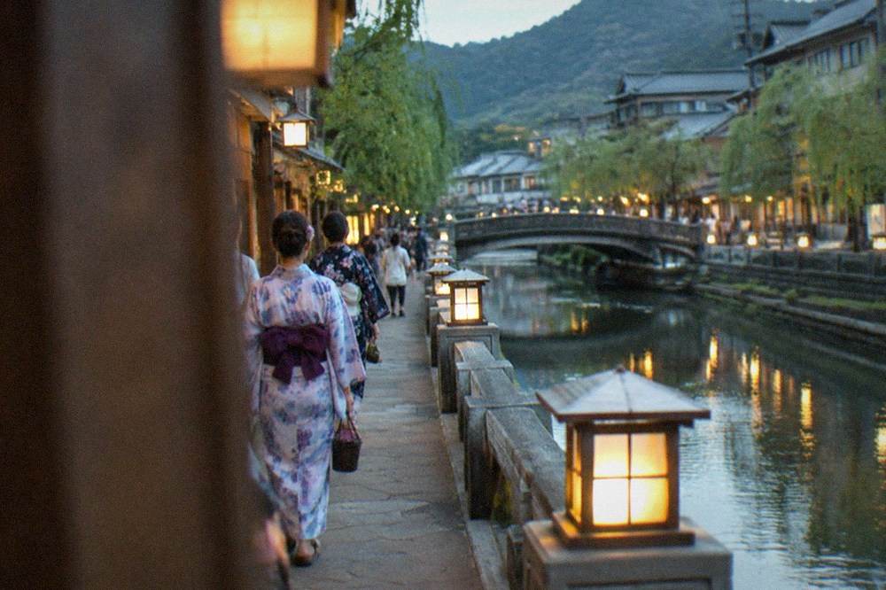 Guests in yukata walking along a lantern-lit canal in the evening