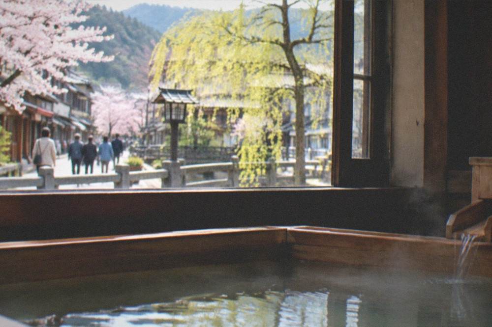 A small wooden bath filled with steaming hot spring water beside a window