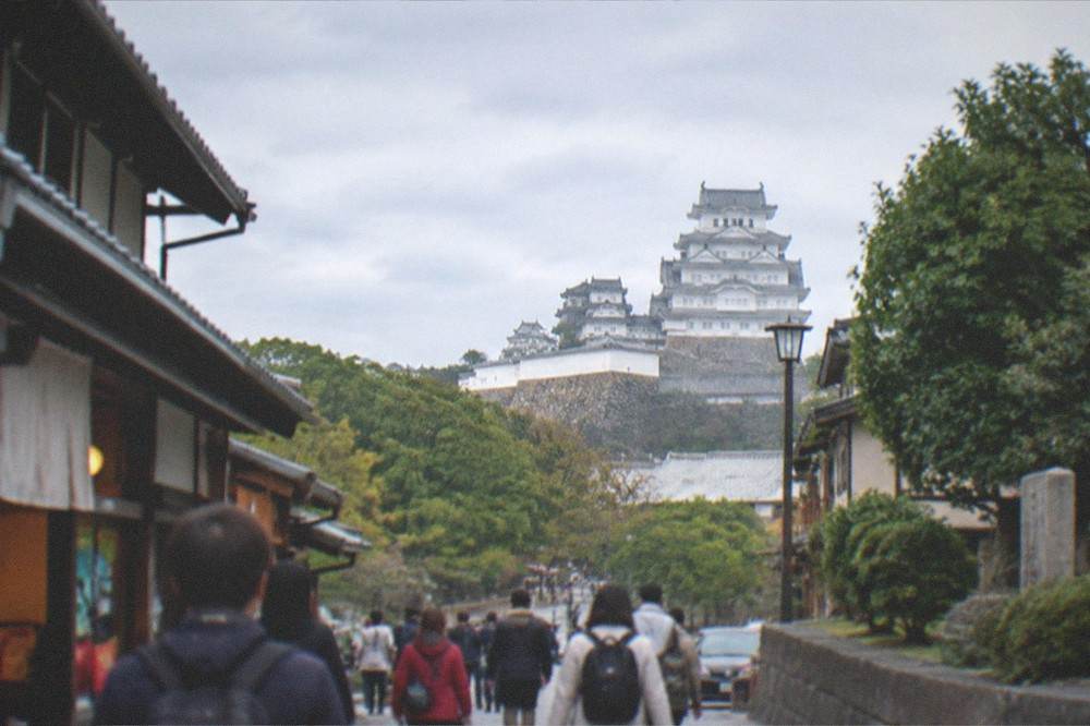 White multi-storey castle keep rising above trees at Himeji