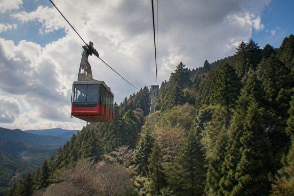 Red and grey cable car ascending a steep forested mountainside track