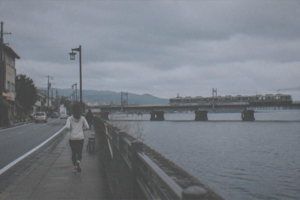 A commuter train crossing a rail bridge over the edge of a wide lake in soft light