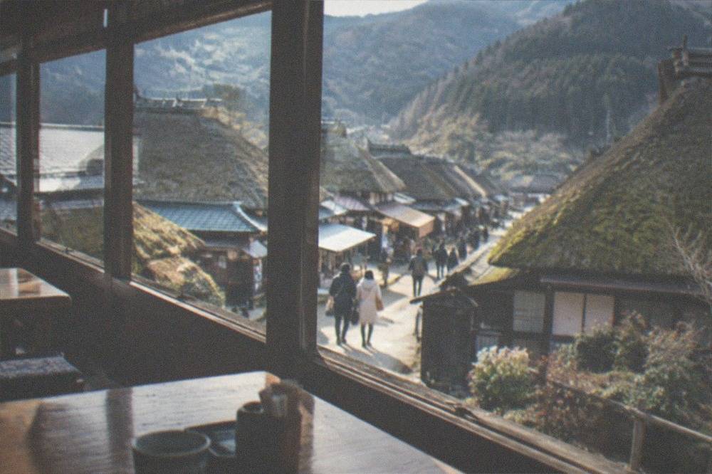 A simple mountain restaurant interior with wooden tables and a view of a thatched village street