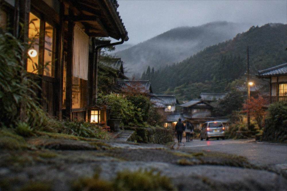 A farmhouse guesthouse at dusk with warm light in the windows and mist over the valley