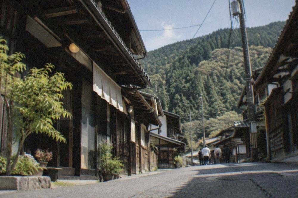 A quiet mountain village street in Ohara with traditional wooden houses and forested hills behind them