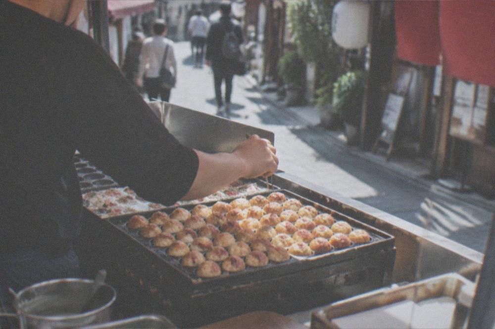 A cook turning takoyaki balls in a cast-iron griddle pan at a street stall