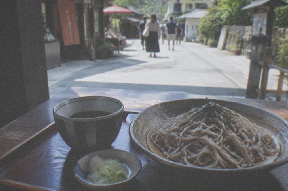A bowl of cold soba noodles with dipping sauce on a wooden tray