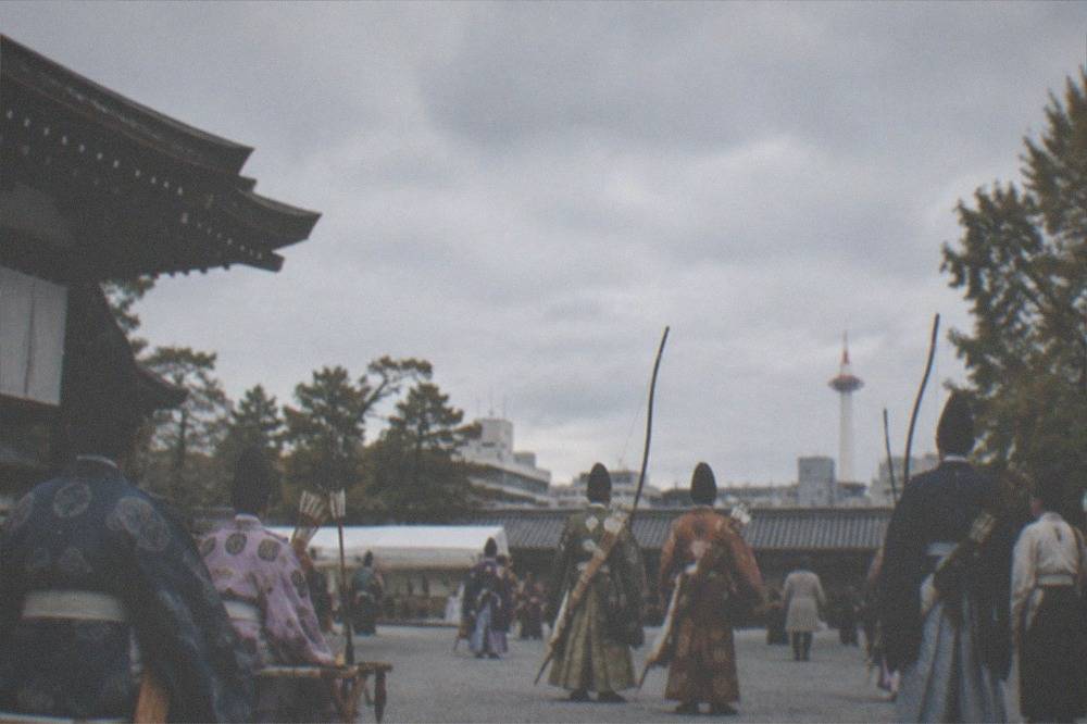 Rows of costumed archers and courtiers resting in a shrine courtyard between rites