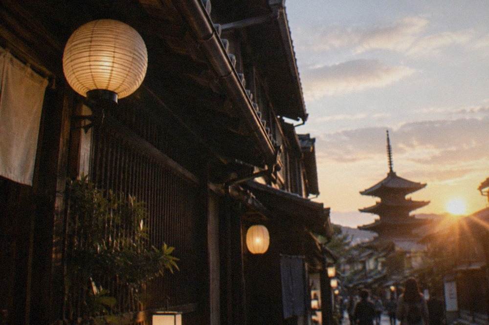 A traditional Kyoto street at dusk with wooden machiya facades and lanterns glowing