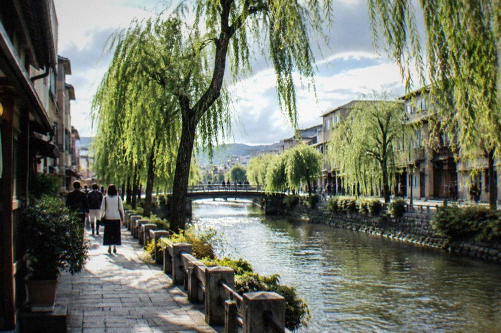A canal lined with willow trees in central Kyoto with pedestrians on the towpath