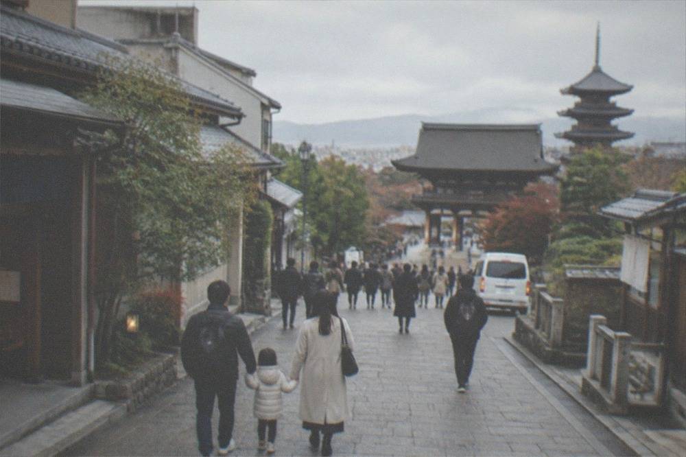 A wide stone-paved street in Kyoto with a family walking and temples in the background