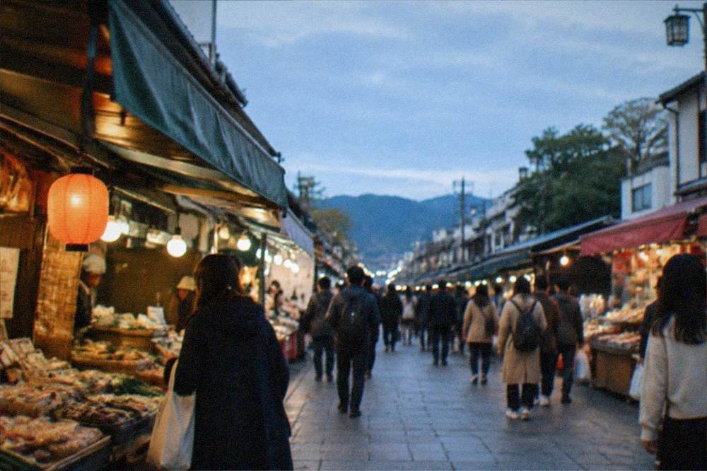 A busy Kyoto food market lane in daytime with shoppers browsing covered stalls