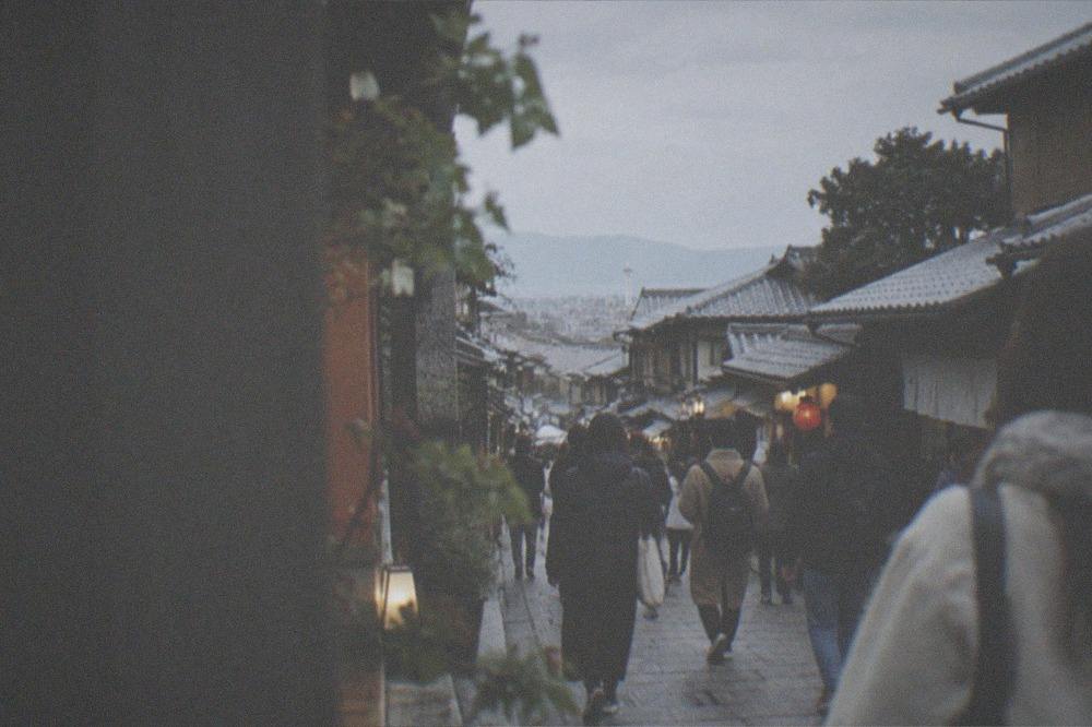 A crowded stone approach street in Kyoto with visitors walking between traditional shopfronts