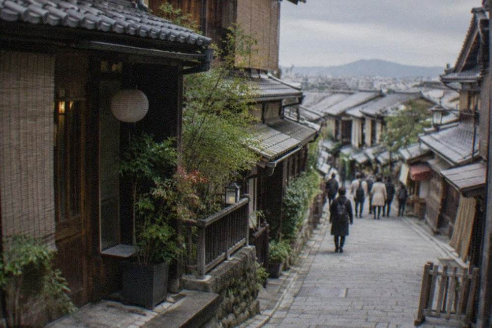 A narrow Gion street at dusk with paper lanterns glowing along traditional wooden facades