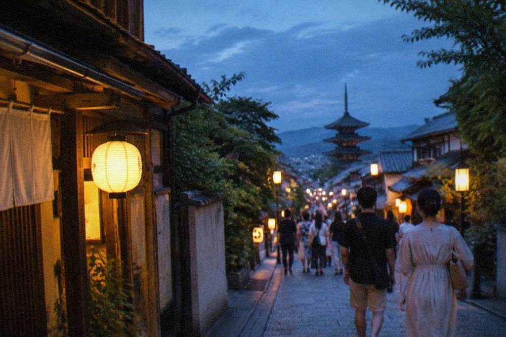 Crowds of people in summer dress walking along a lantern-lit Kyoto street at night