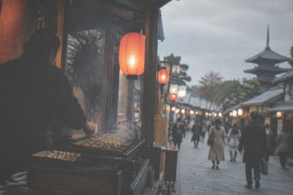 Food stall vendors grilling skewers beside a lantern-lit festival street