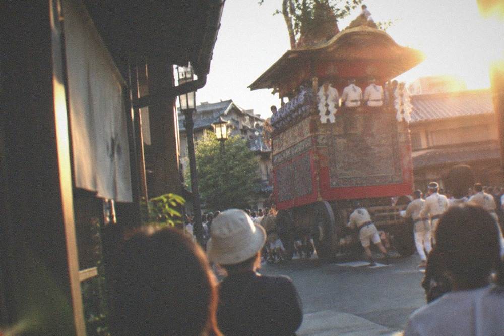 A hand-pulled festival float turning a corner on a city street watched by a crowd