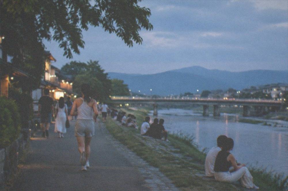 People in light summer clothing waiting along a riverside path in Kyoto at dusk