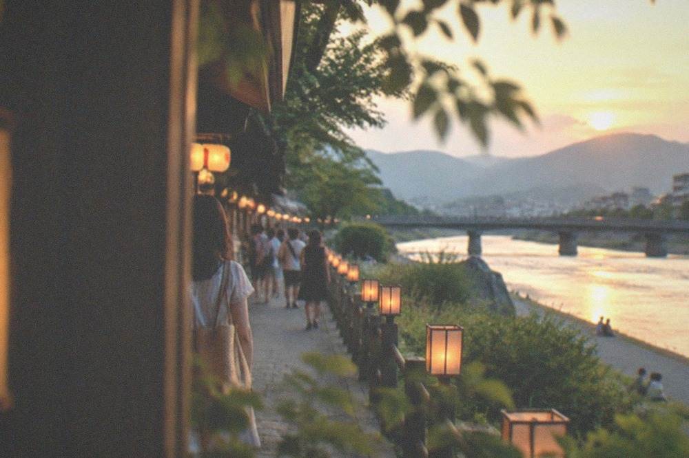 Lanterns glowing along a riverside walkway in Kyoto on a summer evening