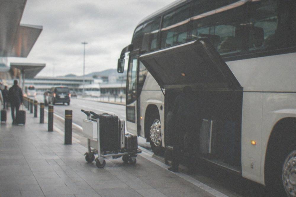 A highway coach parked at an airport curb with luggage being loaded into its hold