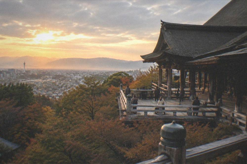 A wooden temple stage overlooking a city skyline at golden hour with hills behind